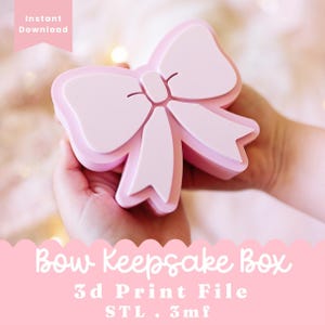 Puede incluir: Una caja de recuerdos de color rosa claro con forma de lazo y tapa extraíble. El texto en la imagen dice Instant Download, Bow Keepsake Box, 3d Print File, STL . 3mf. El objeto presenta una superficie lisa y un diseño dimensional en capas.