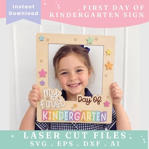 Op de afbeelding: Een rechthoekige houten fotolijst met de tekst My First Day Of Kindergarten in gelaagde script- en blokletters. Het frame is versierd met kleine uitgesneden sterren in pastelkleuren zoals roze, paars, geel en groen.