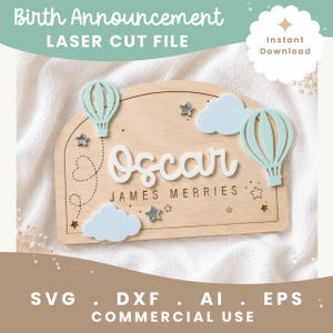 May include: A wooden arch-shaped birth announcement sign featuring the name Oscar in white script, the name James Merries in black text, two light blue hot air balloons, two light blue clouds, and several small silver and gold star cutouts.