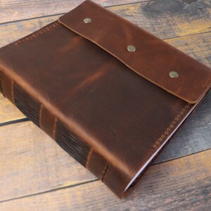 May include: A brown leather-bound journal with a flap closure and metal accents. The journal has a rustic, vintage look.