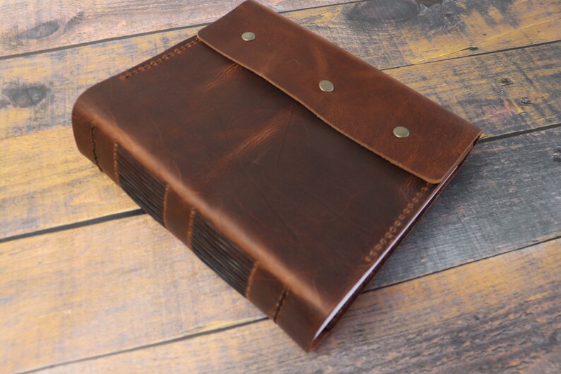 May include: A brown leather-bound journal with a flap closure and metal accents. The journal has a rustic, vintage look.