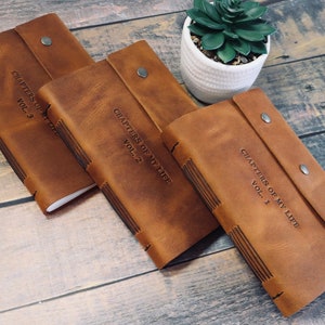 May include: Three brown leather journals with the text "Chapters of My Life" and volume numbers 1, 2, and 3 embossed on the covers.