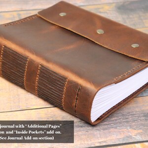 May include: A brown leather-bound journal with a flap closure and stitching detail. The journal has blank pages and a rustic appearance.