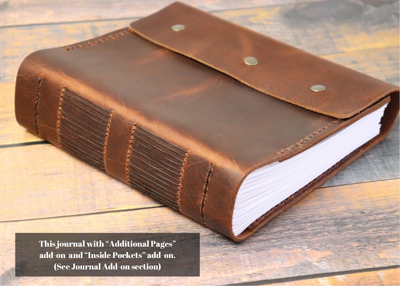 May include: A brown leather-bound journal with a flap closure and stitching detail. The journal has blank pages and a rustic appearance.