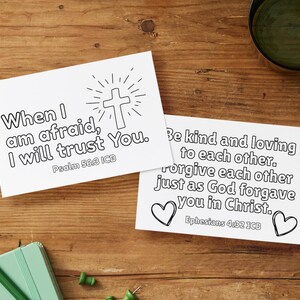 May include: Two white cards with black text and illustrations on a wooden surface. One card reads "When I am afraid, I will trust You." with a cross illustration. The other card says "Be kind and loving to each other." with heart illustrations.