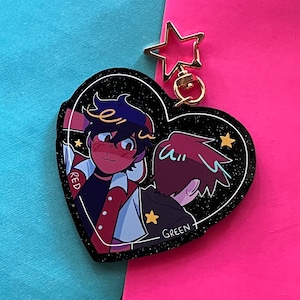 以下が含まれることがあります： キラキラ光る黒いハート型のキーホルダーには、2人の漫画のキャラクターが描かれています。左側のキャラクターは、白いドットの赤いシャツと、黄色い星がついた青い帽子をかぶっています。右側のキャラクターは、緑の星がついた黒いシャツを着ています。キャラクターの下には「RED」と「GREEN」の文字が書かれています。キーホルダーには、金の星のチャームが付いています。