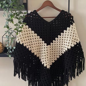 May include: Black and cream crochet poncho with fringe. The poncho is made with a simple stitch pattern and has a V-neck.