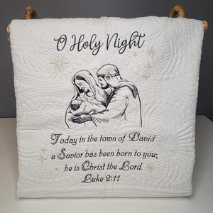 May include: White quilted blanket featuring the text "O Holy Night" and an embroidered image of Mary, Joseph, and baby Jesus. The blanket also includes the text "Today in the town of David a Savior has been born to you; he is Christ the Lord. Luke 2:11."