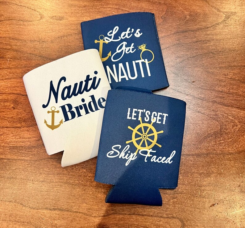 May include: Three navy blue and white drink koozies with nautical-themed text and graphics. One says "Nauti Bride" with an anchor, another says "Let's Get Nauti" with an anchor and ring, and the third says "Let's Get Ship Faced" with a ship's wheel.
