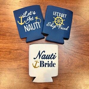 May include: Three navy blue and white can coolers with nautical-themed text and graphics. Two coolers read "Let's Get Nauti" and "Let's Get Ship Faced". The third cooler says "Nauti Bride" with an anchor graphic.
