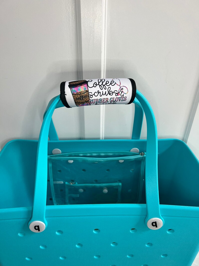 May include: A turquoise tote bag with a handle wrap that reads "Coffee, Scrubs & Rubber Gloves". The bag has a clear interior organizer and white accents. The handle wrap features a coffee cup design.