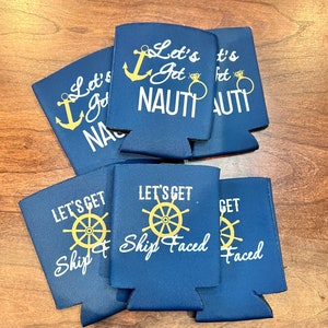 May include: Navy blue drink koozies with white and gold text. The koozies have nautical themes, with phrases like "Let's Get Nauti" with an anchor and ring graphic, and "Let's Get Ship Faced" with a ship's wheel.