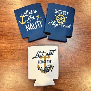May include: Three nautical-themed can coolers. Two are navy blue with white and gold text that reads "Let's Get Nauti" and "Let's Get Ship Faced". The third is white with gold anchor and text that reads "Last Sail Before the Veil!"