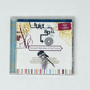 May include: A Built to Spill Ancient Melodies of the Future CD in a clear plastic jewel case. The cover features abstract yellow and maroon line art, a black guitar graphic, and a pink sticker stating Featuring Strange and The Weather.