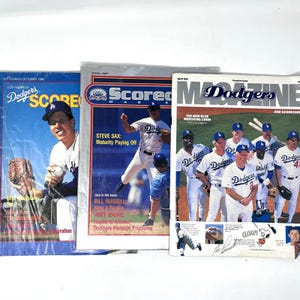 May include: Three vintage Los Angeles Dodgers Scorebook and Magazine publications from 1985, 1987, and 1988. The covers feature professional baseball players in white and blue uniforms, action photography, team logos, and bold text headlines.