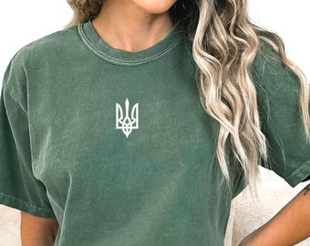 May include: A green t-shirt with a white embroidered Ukrainian trident symbol.