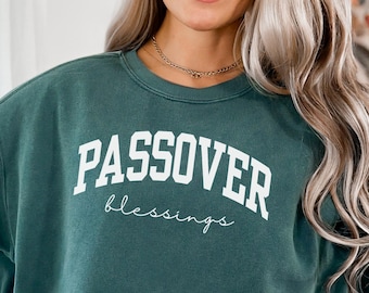 Pode incluir: Uma camisola verde escuro com as palavras "PASSOVER" em letras brancas em negrito acima da palavra "blessings" em uma fonte cursiva. A camisola é de gola redonda.