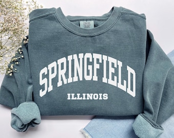 May include: A teal blue sweatshirt with white text that reads "SPRINGFIELD ILLINOIS" in an arched font.