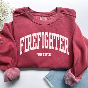 May include: A maroon sweatshirt with the text "FIREFIGHTER WIFE" in white.