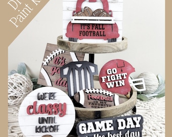 Puede incluir: Kit de pintura DIY con recortes de madera con temática de fútbol americano. Incluye un camión rojo con balones, una camiseta de árbitro, un casco y letreros con frases como "It's Fall Football", "Go Fight Win" y "Game Day is the best day".