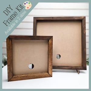 May include: Two square wooden DIY frame kits in different sizes. The frames are stained a dark brown and have a natural-colored backing. The text "DIY Frame Kit" and "Available in 2 sizes" is printed on the top left corner.