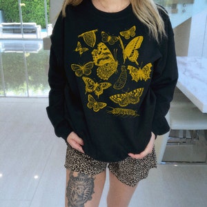 May include: Black sweatshirt with a yellow graphic print of various butterflies and insects.