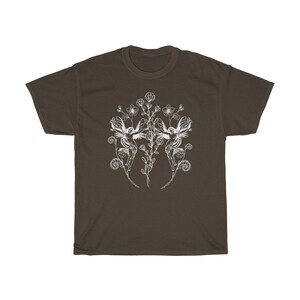 May include: A brown t-shirt featuring a white illustration of two fairies with floral elements. The design includes flowers, leaves, and swirling details, creating a whimsical and artistic aesthetic. The shirt is made of a soft material.