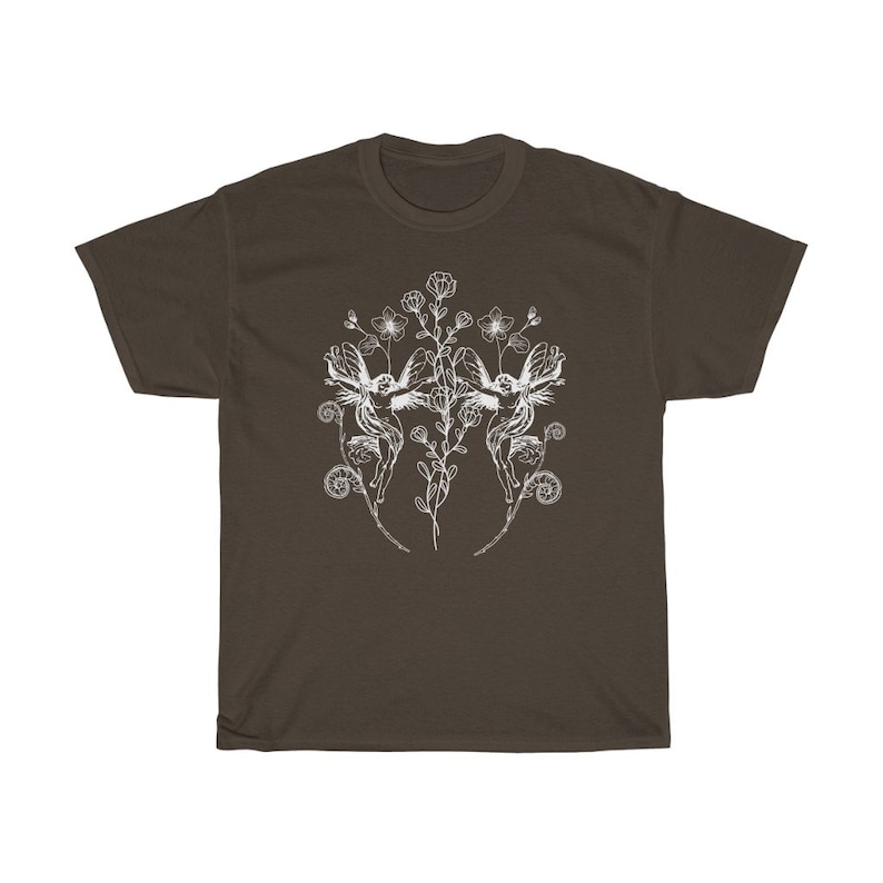 May include: A brown t-shirt featuring a white illustration of two fairies with floral elements. The design includes flowers, leaves, and swirling details, creating a whimsical and artistic aesthetic. The shirt is made of a soft material.