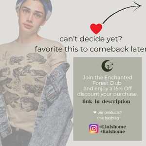 May include: A beige t-shirt with a graphic print of frogs and mushrooms. The text "can't decide yet? favourite this to comeback later." is displayed above a green rectangle with a crescent moon and stars. The text inside the rectangle reads "Join the Enchanted Forest Club and enjoy a 15% Off discount your purchase. link in description. our products? use hashtag @Liaishome #liaishome"