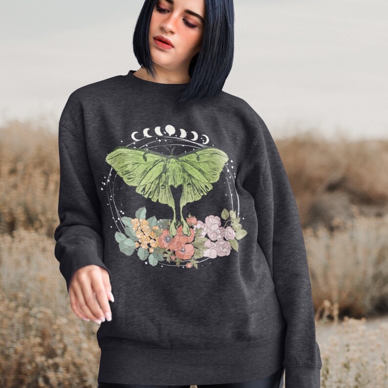 May include: A dark grey sweatshirt with a green luna moth graphic. The moth is surrounded by a circle of flowers and crescent moons.