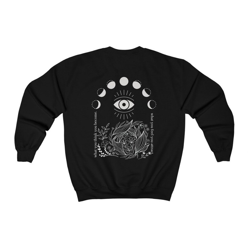 Op de afbeelding: Zwarte sweatshirt met een wit grafisch ontwerp op de rug. Het ontwerp bevat een oog, maanfasen, bloemelementen en de teksten "what you think you become" en "what you feel you attract."