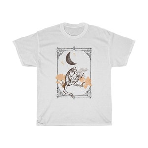 K&ouml;nnte beinhalten: Wei&szlig;es T-Shirt mit einem Grafikdruck einer auf einer zunehmenden Mondsichel sitzenden Kr&ouml;te mit Blumen. Die Grafik ist in einem Vintage-Stil gerahmt.