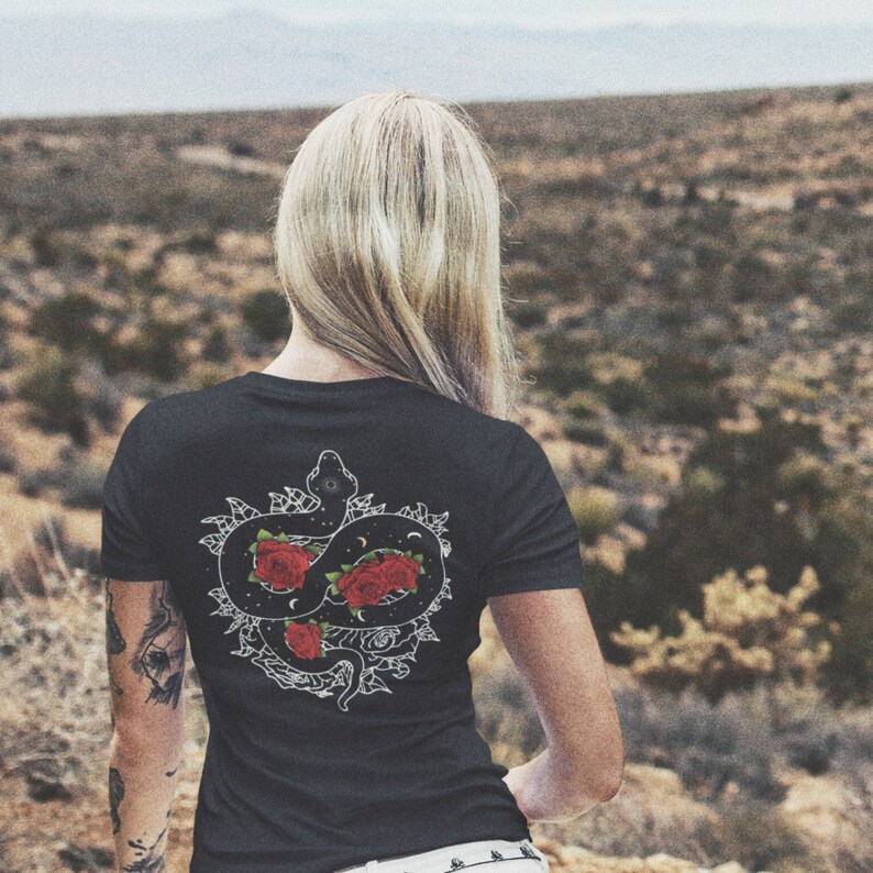 May include: Black t-shirt featuring a white graphic of a snake entwined with red roses and a crescent moon.