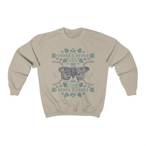 May include: A beige sweatshirt with a blue and green patterned design featuring a moth and geometric shapes.