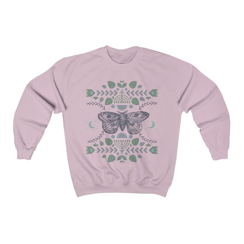 May include: A pink sweatshirt with a graphic design of a moth with wings spread, surrounded by a pattern of leaves, flowers, and geometric shapes in shades of green and blue.