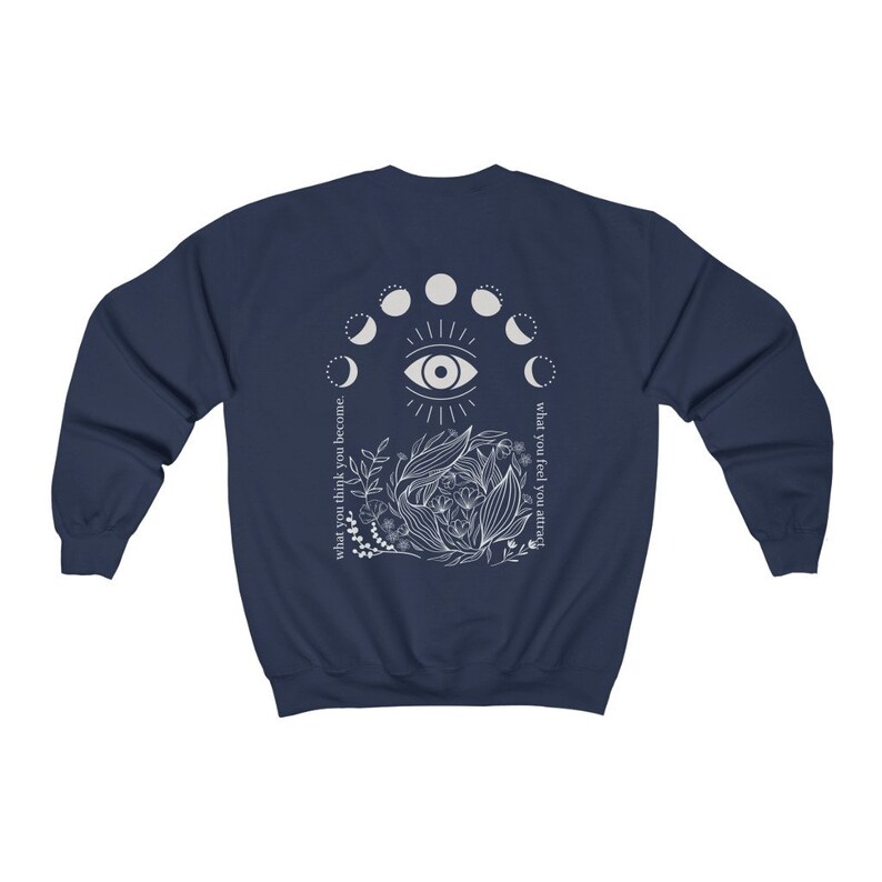 Op de afbeelding: Marineblauw sweatshirt met een wit grafisch ontwerp. Het ontwerp toont een centraal oog, maanfasen, bloemelementen en de teksten "what you think you become" en "what you feel you attract".