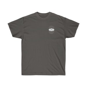 May include: A charcoal gray t-shirt with a white eye design. The eye has a white pupil and is surrounded by radiating lines.