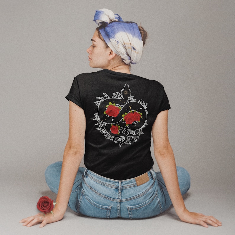 May include: Black t-shirt featuring a white graphic of a snake entwined around red roses. The snake has a third eye on its forehead and is surrounded by stars and moons.