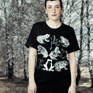 May include: A black t-shirt with a white graphic print of frogs. The frogs are in various poses and sizes, and some have spots.