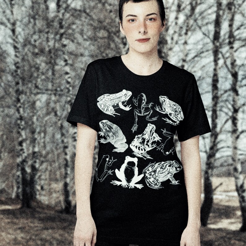 May include: A black t-shirt with a white graphic print of frogs. The frogs are in various poses and sizes, and some have spots.