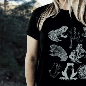 May include: A black t-shirt with a white graphic print of various frogs and toads. The frogs are in different poses, some are jumping, some are sitting, and some are swimming. The shirt is a casual style and would be a great addition to any frog lover's wardrobe.