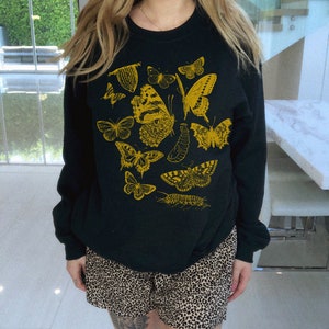 May include: Black sweatshirt with a yellow graphic print of butterflies and other insects.