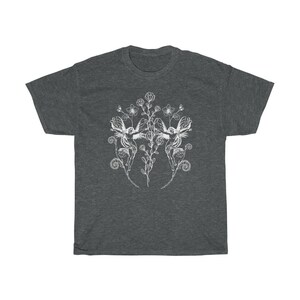 May include: Dark heather gray t-shirt featuring a white illustration of two winged figures surrounded by flowers and foliage. The design is symmetrical, with the figures facing each other. The shirt has a classic crew neck and short sleeves.