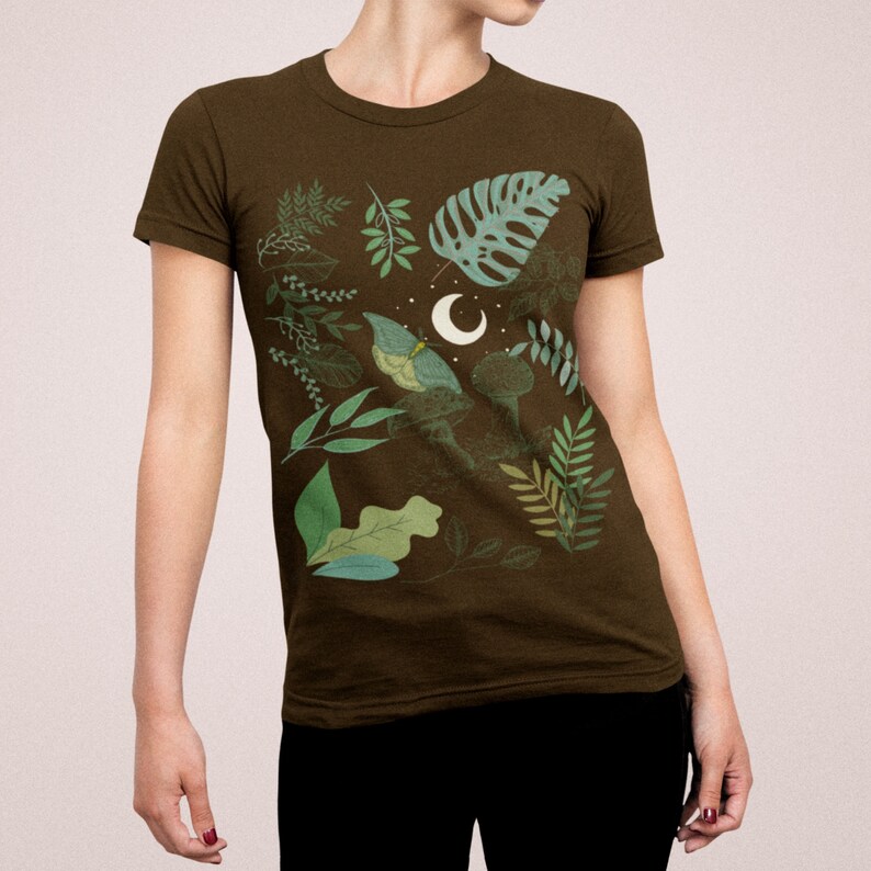 May include: A brown t-shirt with a green and white floral print featuring a crescent moon and a butterfly.
