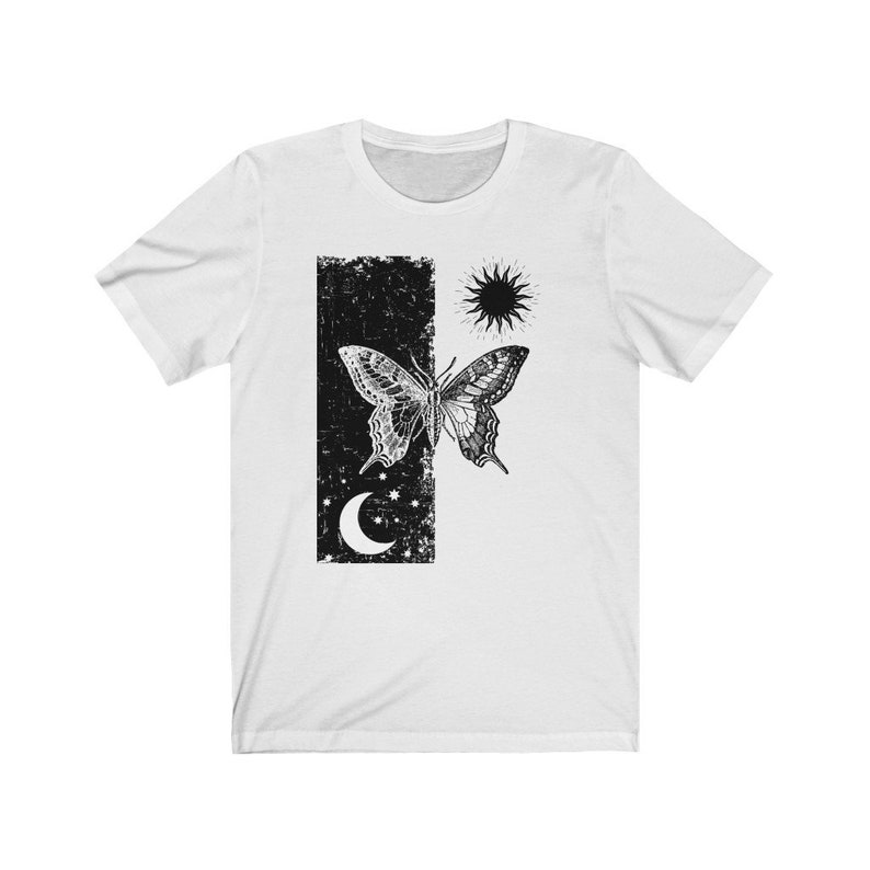 May include: White t-shirt with a black and white graphic print of a butterfly, a sun, a moon, and stars. The graphic is in a distressed style.