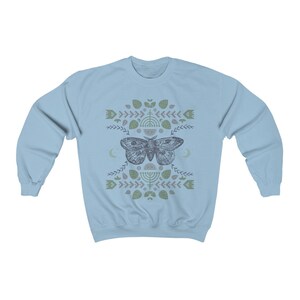 May include: Light blue sweatshirt with a graphic print of a moth with geometric patterns and symbols in shades of green and gray.