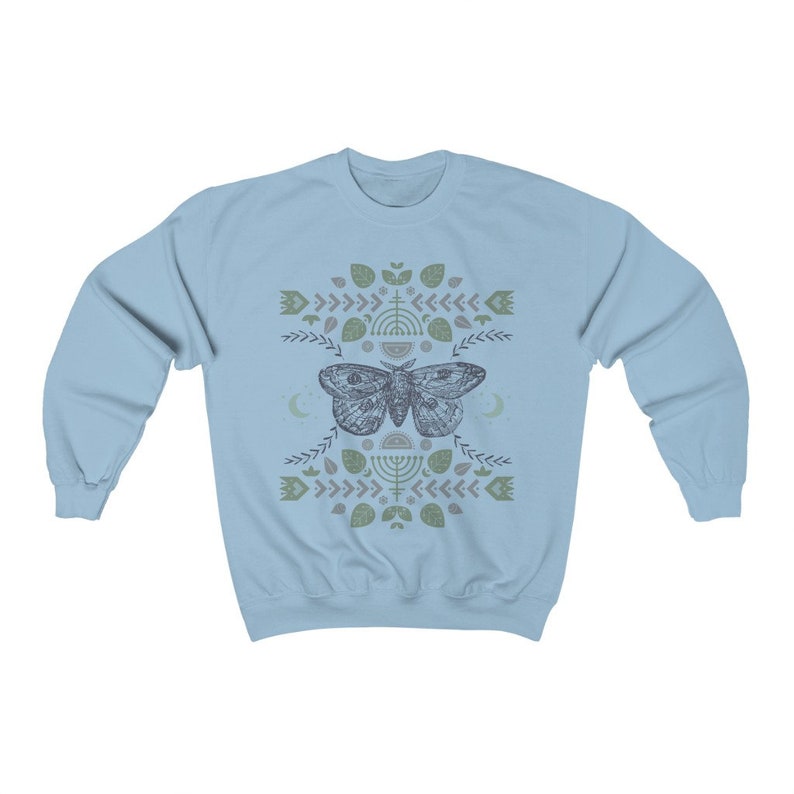 May include: Light blue sweatshirt with a graphic print of a moth with geometric patterns and symbols in shades of green and gray.