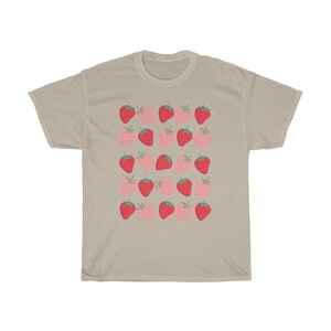 May include: A beige t-shirt with a repeating pattern of red and pink strawberries. The strawberries are stylized and have green leaves.