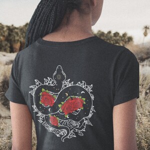 May include: Black t-shirt featuring a white graphic of a snake entwined with roses. The snake is outlined in white and filled with black, while the roses are red with white outlines.