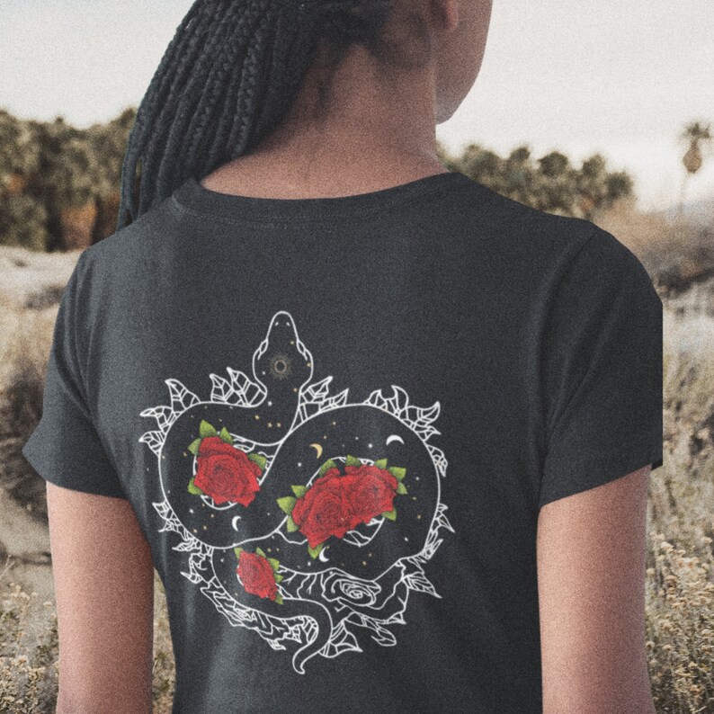 May include: Black t-shirt featuring a white graphic of a snake entwined with roses. The snake is outlined in white and filled with black, while the roses are red with white outlines.